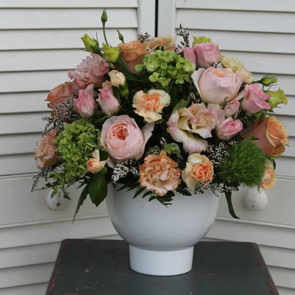 Low white vase of pink and peach roses and carnations with green hydrangea accents