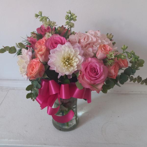 Pink and peach flower arrangement in a glass vase with a magenta ribbon