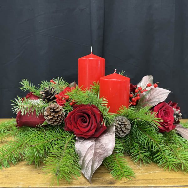 Red roses with pine branches and two red candles on a low centerpiece