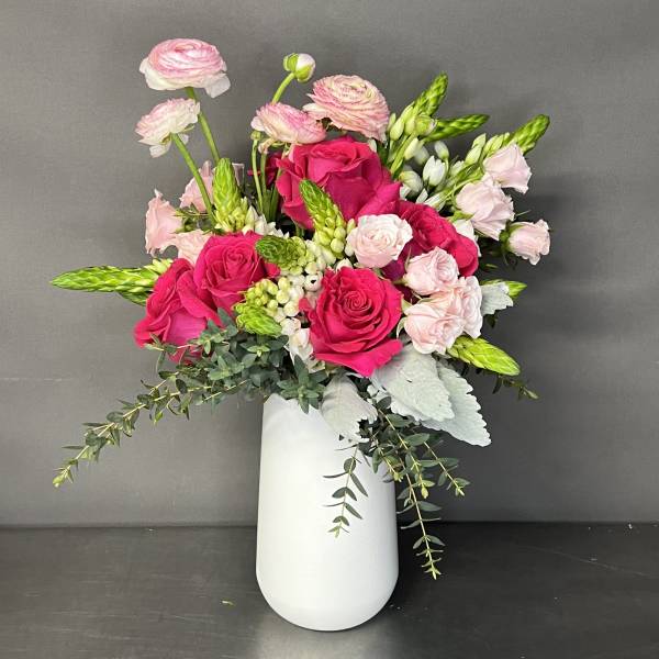 Pink roses and ranunculus in a white vase with trailing greenery