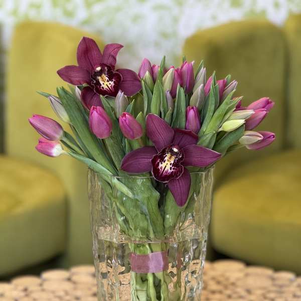 Purple orchids and pink tulips in a clear glass vase
