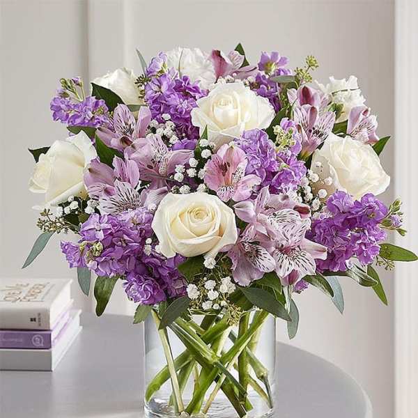 Bouquet of white roses and purple flowers in a clear glass vase