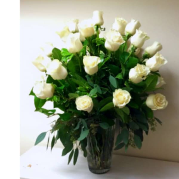 White roses arranged in a clear glass vase with lush greenery