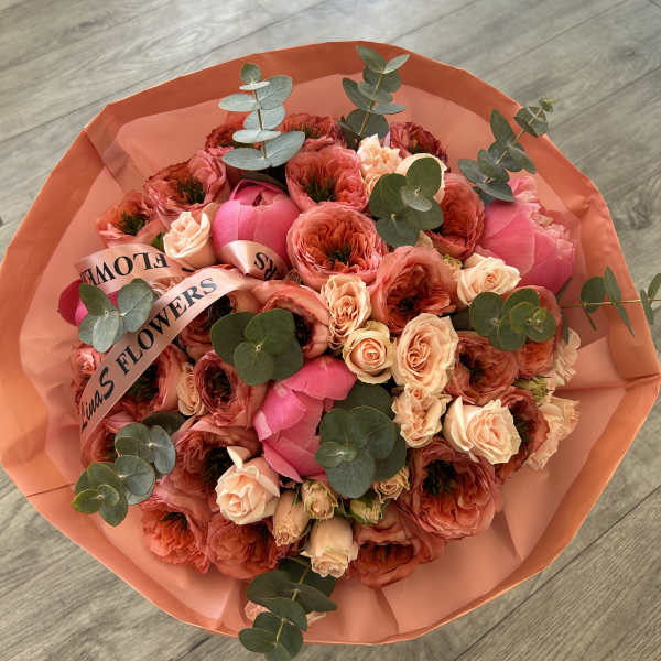 Bouquet of pink and peach roses wrapped in coral paper
