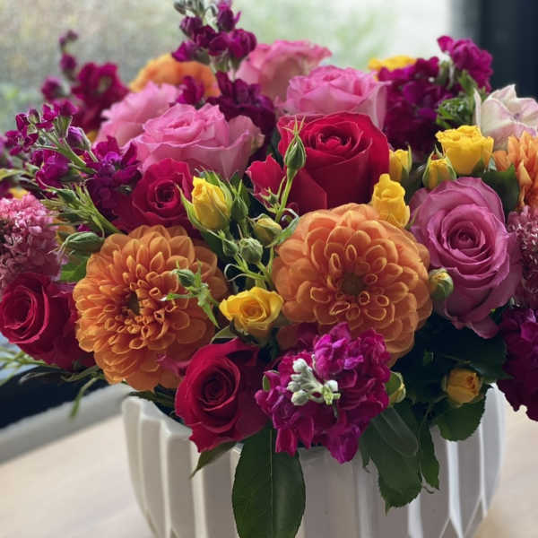 Mixed bouquet of roses, dahlias, and purple blooms in a white vase