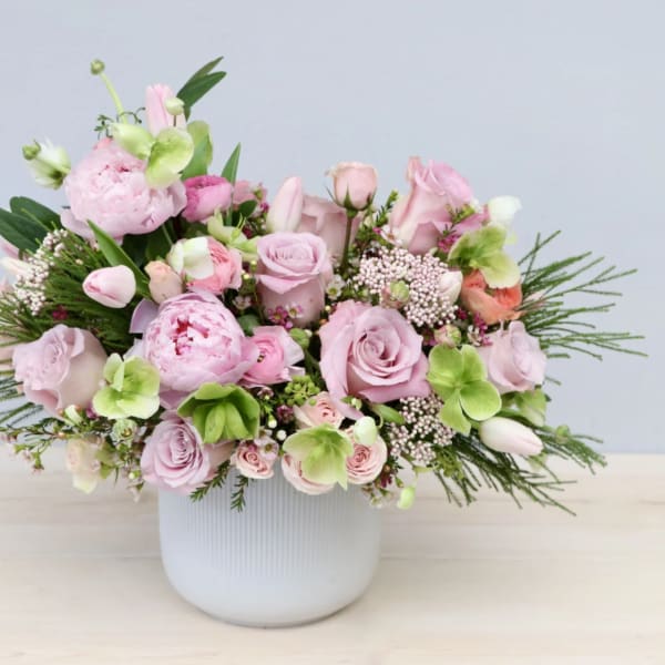 Low white vase filled with pink roses, peonies, tulips and green hydrangea blooms