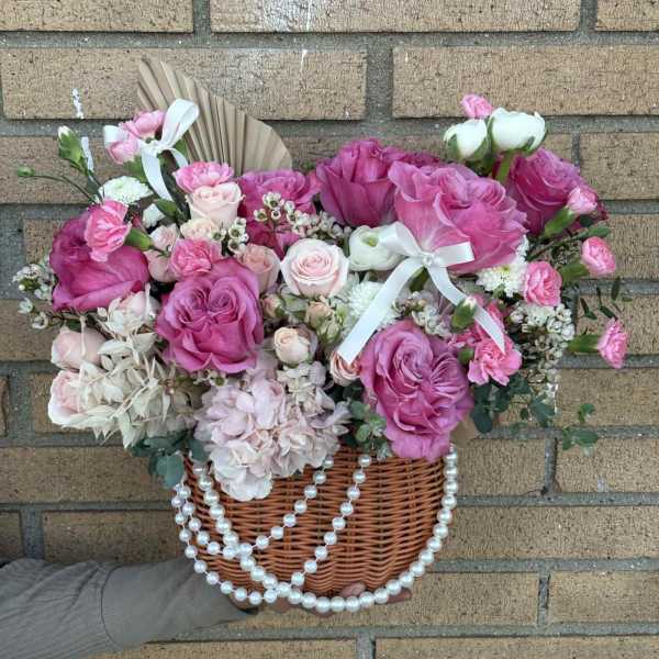 Pink and white rose arrangement in a wicker basket with pearl strands