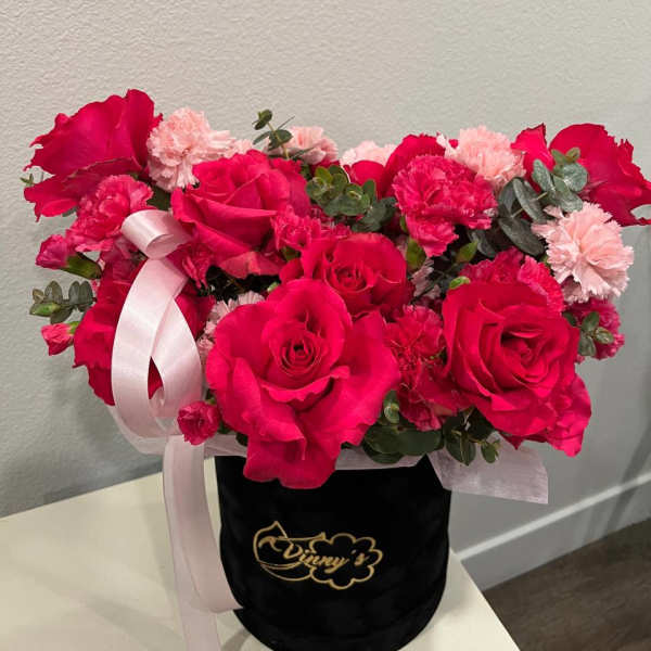 Pink rose and carnation arrangement in a black hat box with ribbon