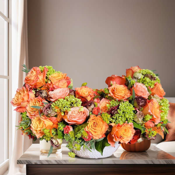 Three orange and peach rose arrangements in low containers on a table
