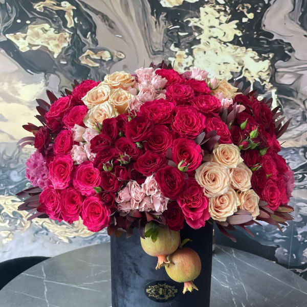 Large bouquet of pink, red, and peach roses in a black box with pomegranates