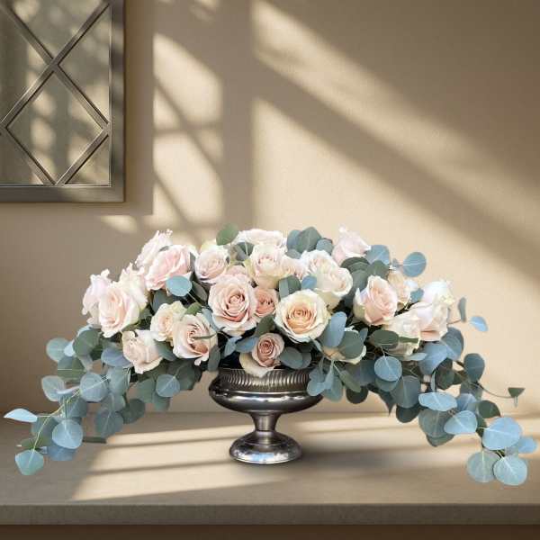 Blush roses arranged in a silver pedestal bowl with trailing eucalyptus
