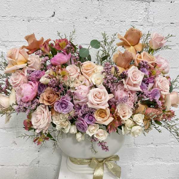 Large pastel rose arrangement in a white vase with a gold ribbon