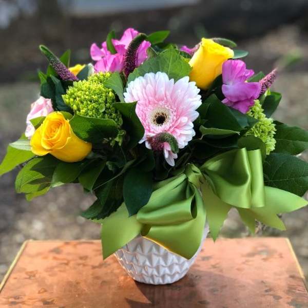Bouquet of yellow roses, pink gerbera daisies, and purple flowers in a white vase
