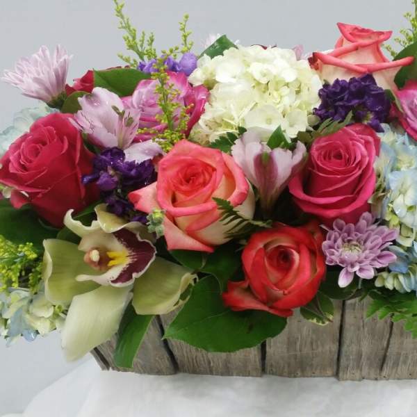 Mixed bouquet of roses, hydrangeas, and orchids in a rustic wooden basket