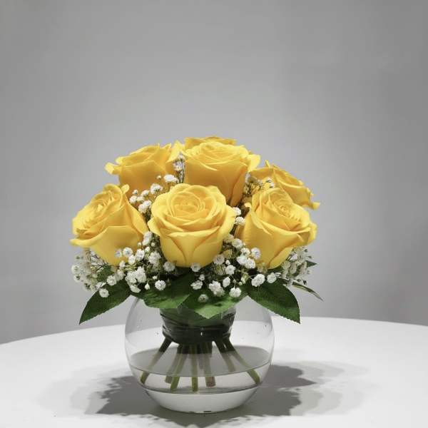 Yellow roses arranged in a clear glass vase with small white filler flowers.