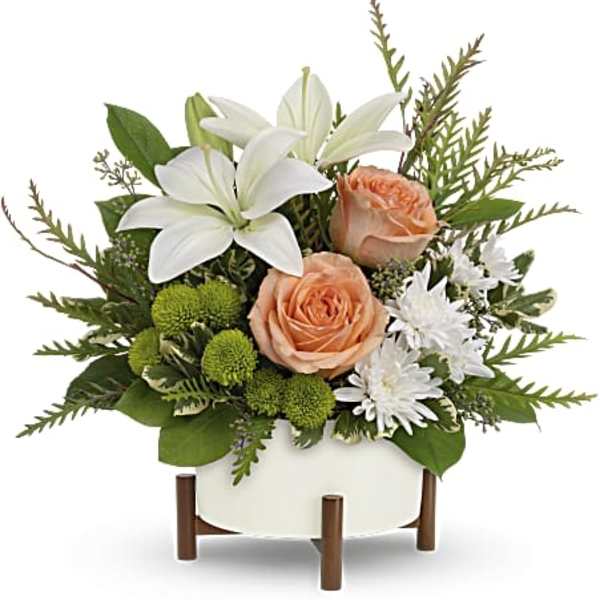 White lilies and peach roses in a white container with green accents