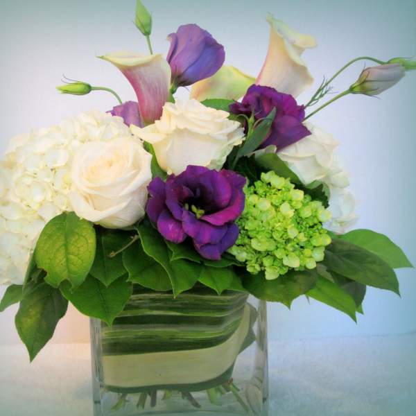 White roses, purple calla lilies, and hydrangeas in a glass vase