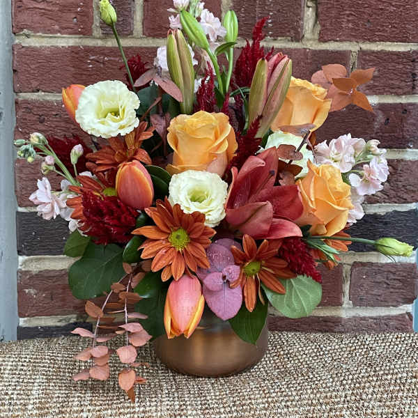 Mixed bouquet with orange roses, lilies, and red flowers in a bronze vase