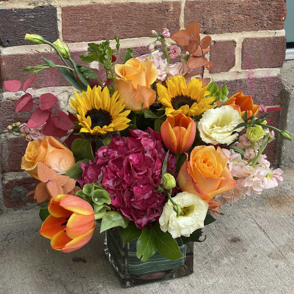 Colorful bouquet with sunflowers, roses, tulips, and hydrangea in a glass vase