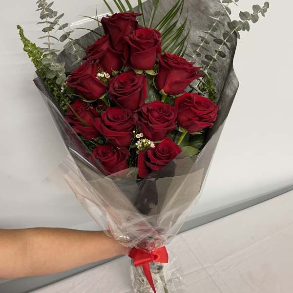 Bouquet of red roses wrapped in dark paper with a red ribbon