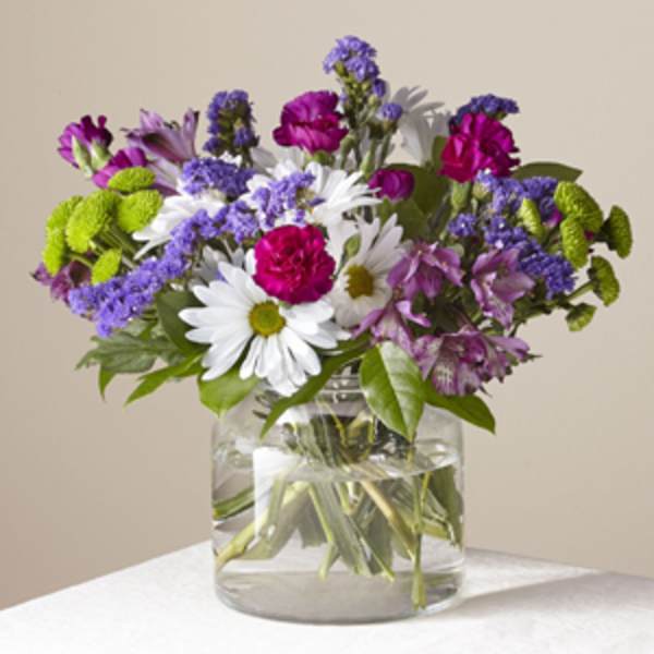 Mixed bouquet of white daisies, pink carnations, and purple flowers in a glass vase