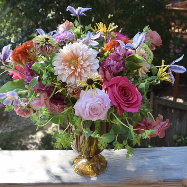 Mixed bouquet of pink, peach, and purple flowers in an amber vase