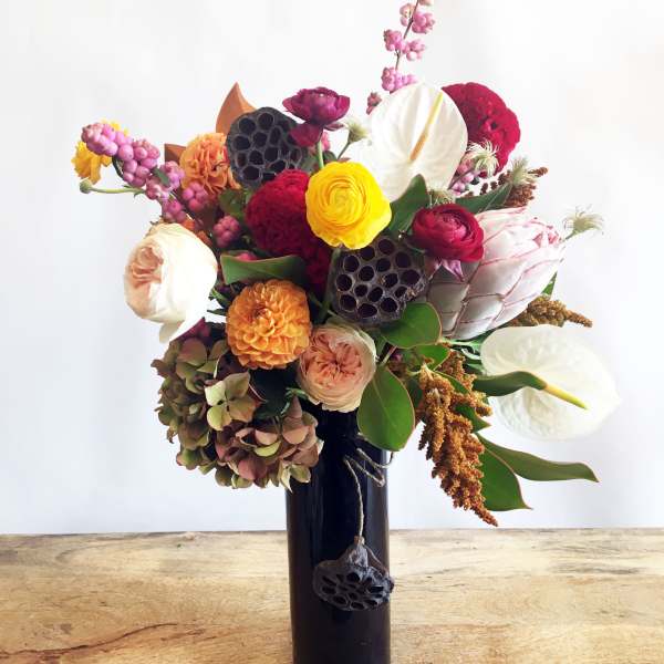 Mixed bouquet with white anthuriums, roses, and bright blooms in a dark vase