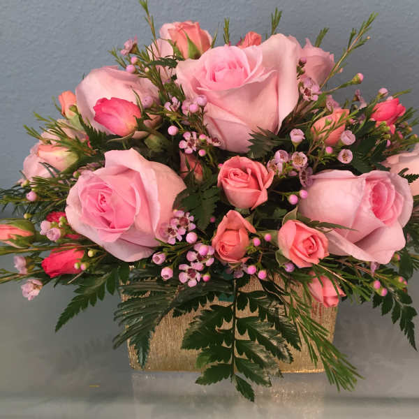 Pink roses and spray roses arranged in a gold rectangular container