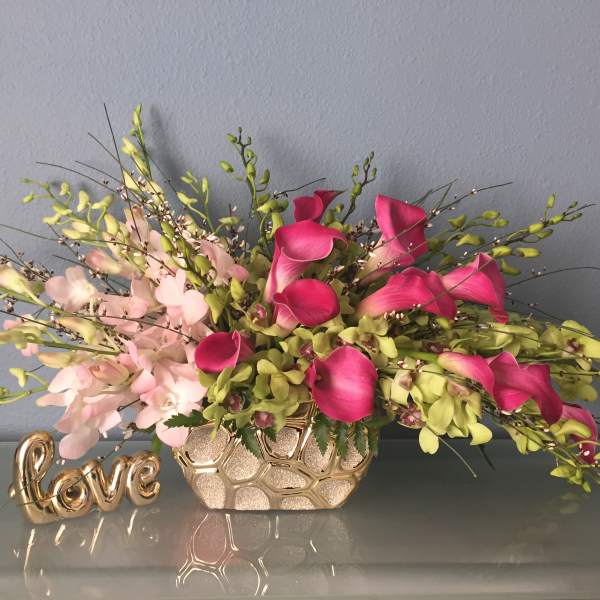 Pink and green floral arrangement in a gold vase beside a decorative "love" sign