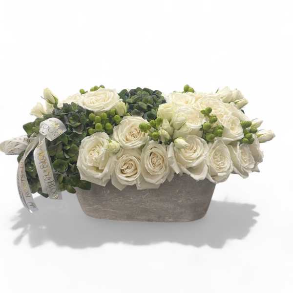 White roses arranged in a low rectangular vase with green berries