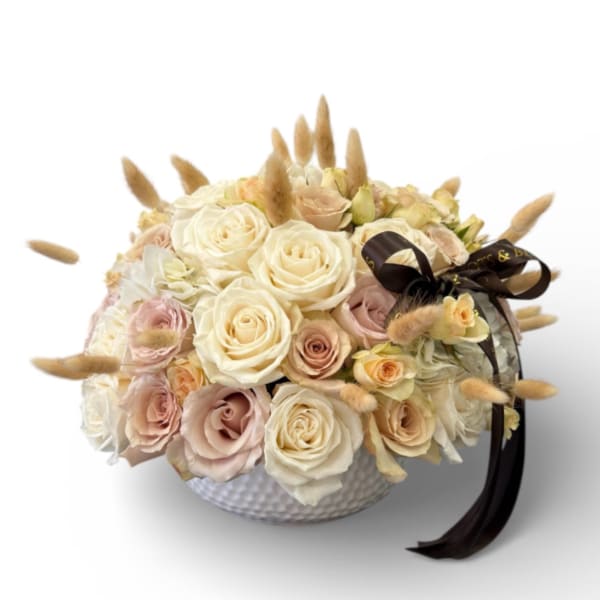 Cream and blush roses in a white textured bowl with a dark ribbon