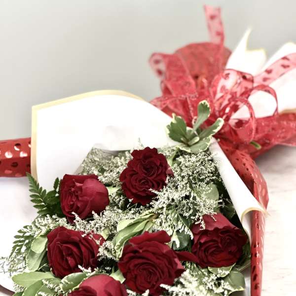 Bouquet of red roses wrapped in white paper with red ribbon