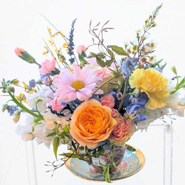 Pastel arrangement of roses, daisies, and mixed blooms in a patterned teacup on a matching saucer