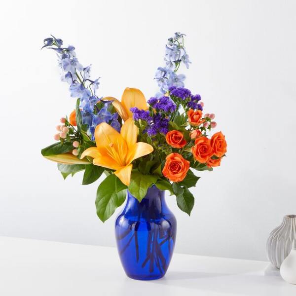 Bouquet of orange roses and yellow lilies in a blue glass vase