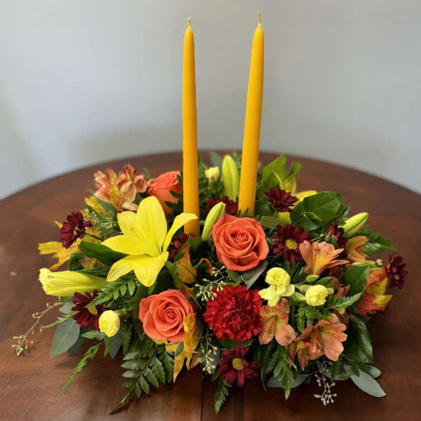Floral centerpiece with two yellow taper candles and mixed blooms in warm colors