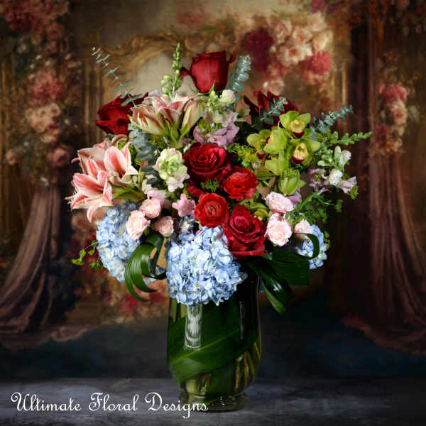 Mixed bouquet of red roses, lilies, and blue hydrangeas in a glass vase
