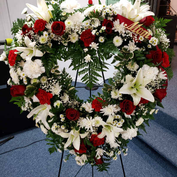 Heart-shaped floral wreath with white lilies, red roses, and white daisies