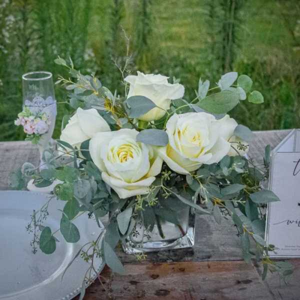 White roses in a clear glass vase with eucalyptus greenery