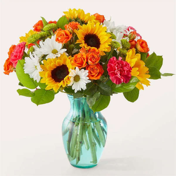 Mixed bouquet of sunflowers, roses, daisies, and carnations in a blue glass vase