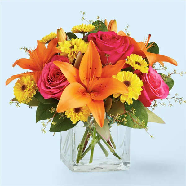 Bouquet of orange lilies, pink roses, and yellow daisies in a clear glass vase