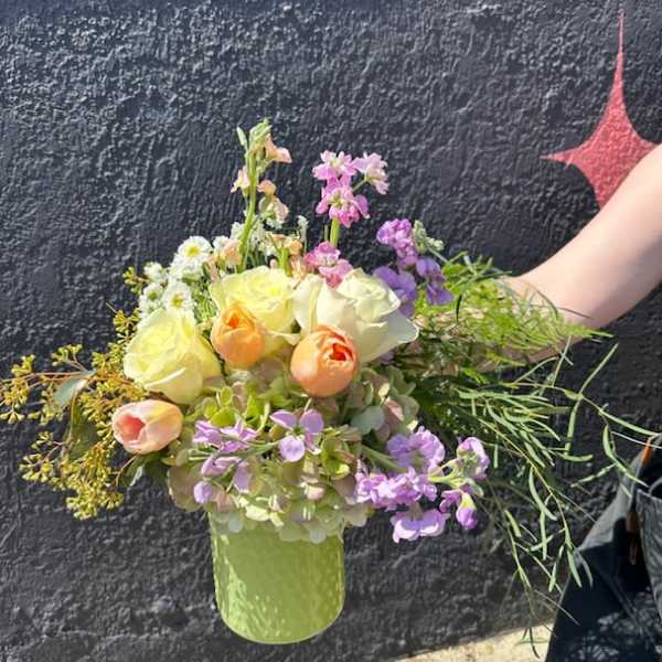 Pastel arrangement of yellow roses, peach tulips, and purple blooms in a light green vase.