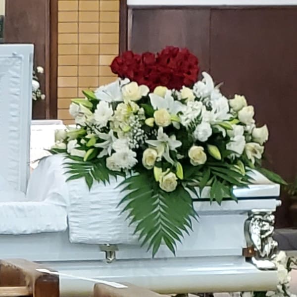 White casket with floral sprays and a white flower wreath in a church