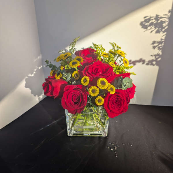Red roses and yellow button flowers in a square glass vase