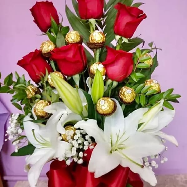 Red roses and white lilies with gold-wrapped chocolates and a red ribbon