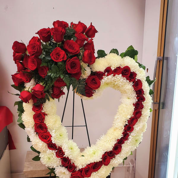 Heart-shaped floral wreath with red roses and white flowers on a stand