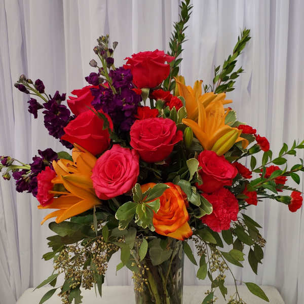Mixed bouquet of red, pink, orange, and purple flowers in a glass vase