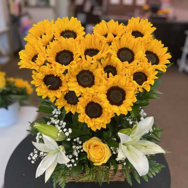 Basket arrangement of yellow sunflowers, white lilies, and a yellow rose