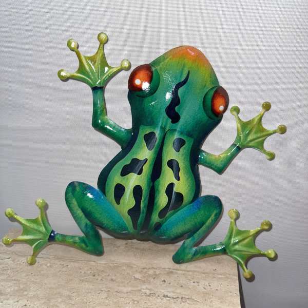 Colorful frog figurine with outstretched legs on a stone surface