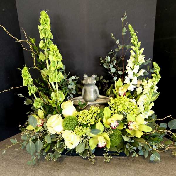 Green floral arrangement with a small frog statue in the center