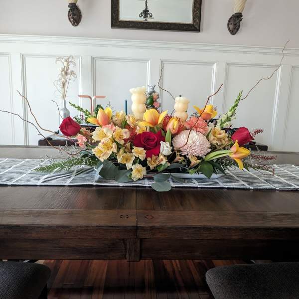 Low floral centerpiece with roses, lilies, and chrysanthemums in warm pink and yellow tones